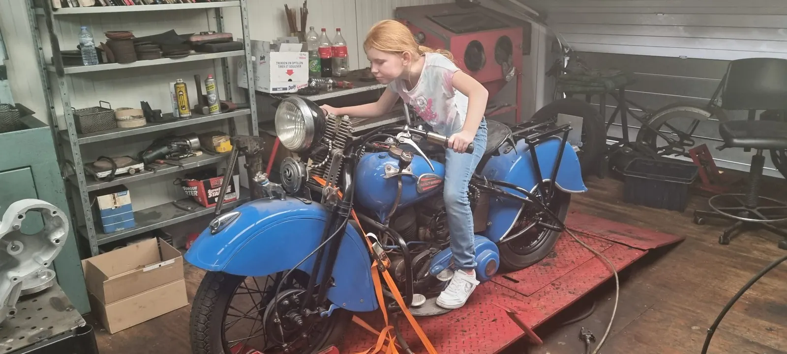 Kind op een oude blauwe Harley in de werkplaats